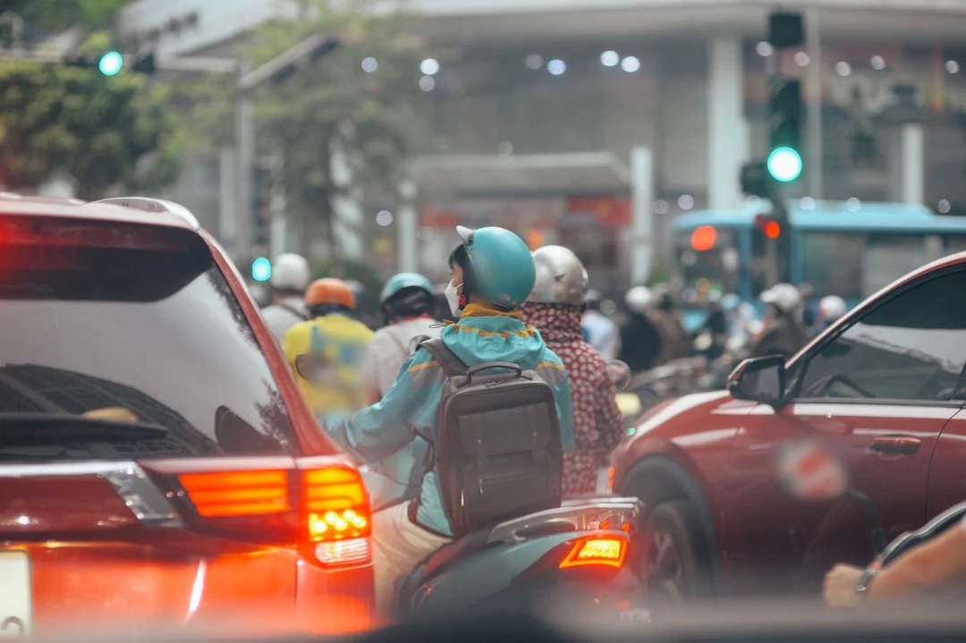 A masked motorbike rider waiting at the lights among cars and motorbikes at rush hour, the air hazy with exhaust
