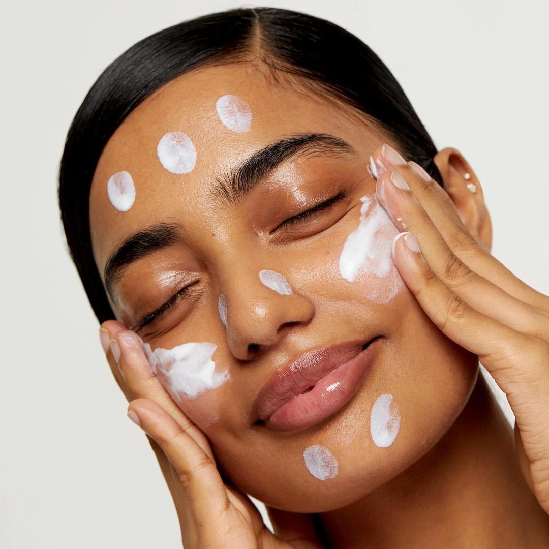 Dots of sunscreen across the face before spreading — sunscreen is the last skincare layer and needs to form a continuous, adequate film